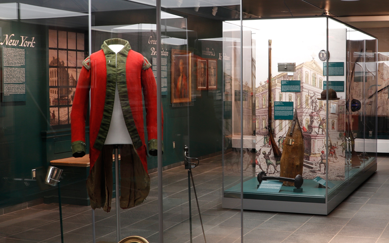A dark green museum gallery with glass cases filled with artifacts