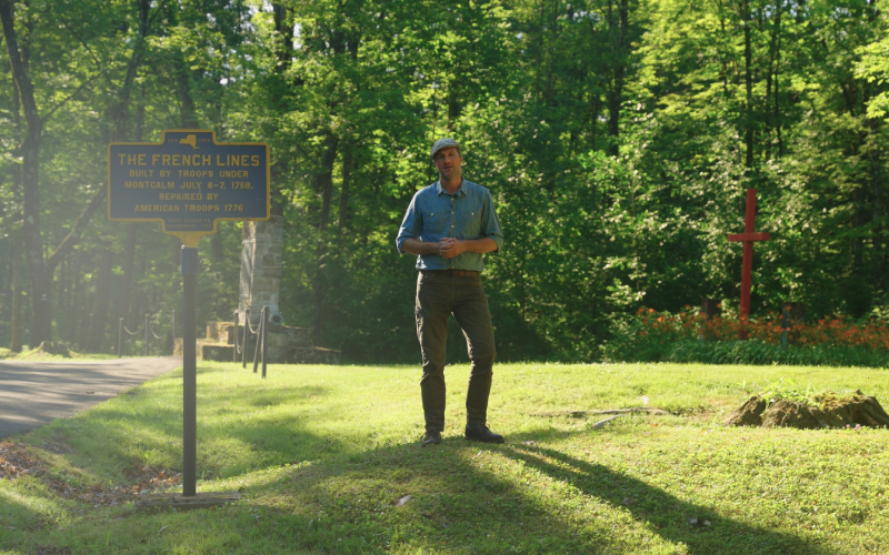 Curator Dr. Matthew Keagle standing next to Liberty Hill sign at battlefield ground at Fort Ticonderoga